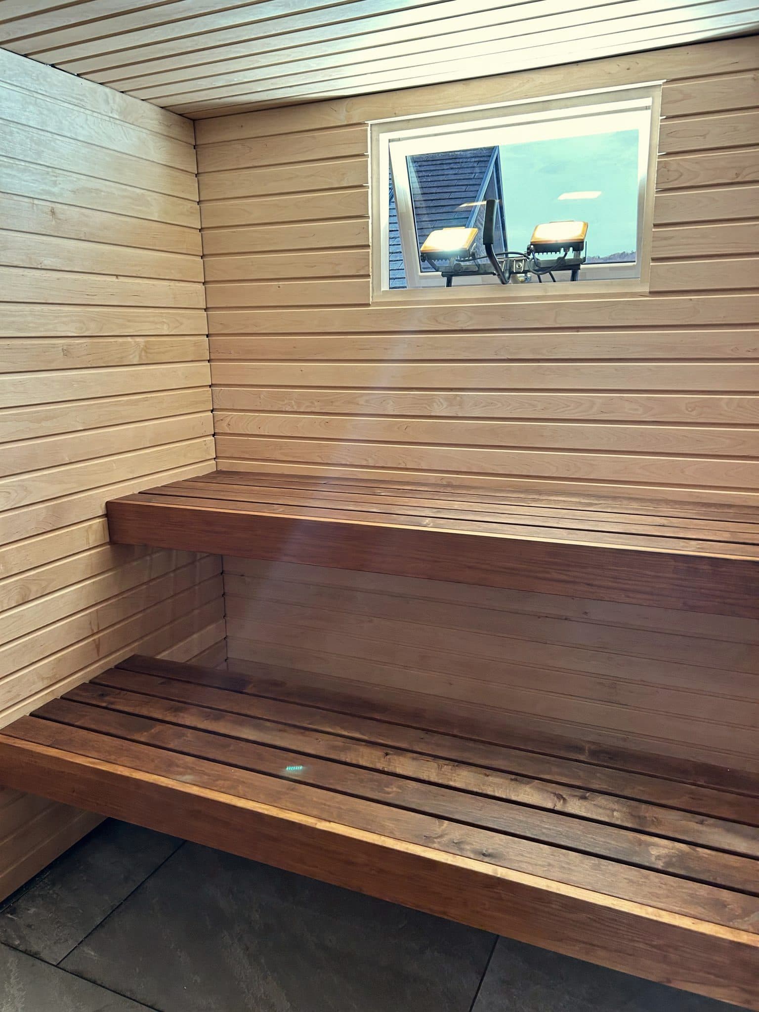 Finished sauna interior with two tiers of dark-stained benches, pale cladding and a small window