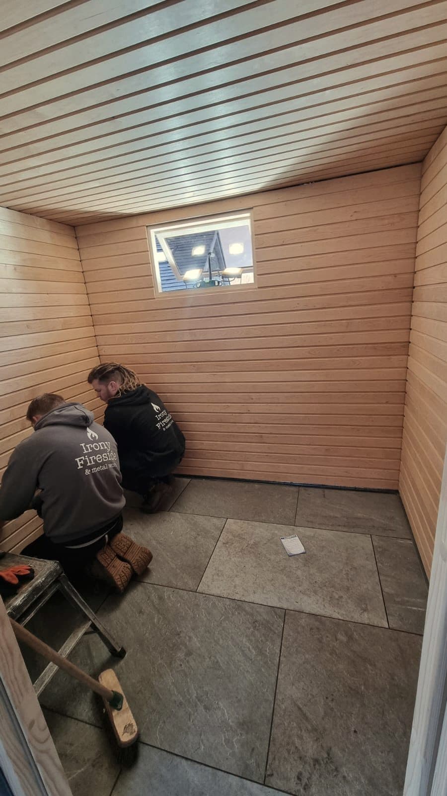 Irony Fireside builders fitting horizontal timber cladding inside the sauna, stone floor tiles laid