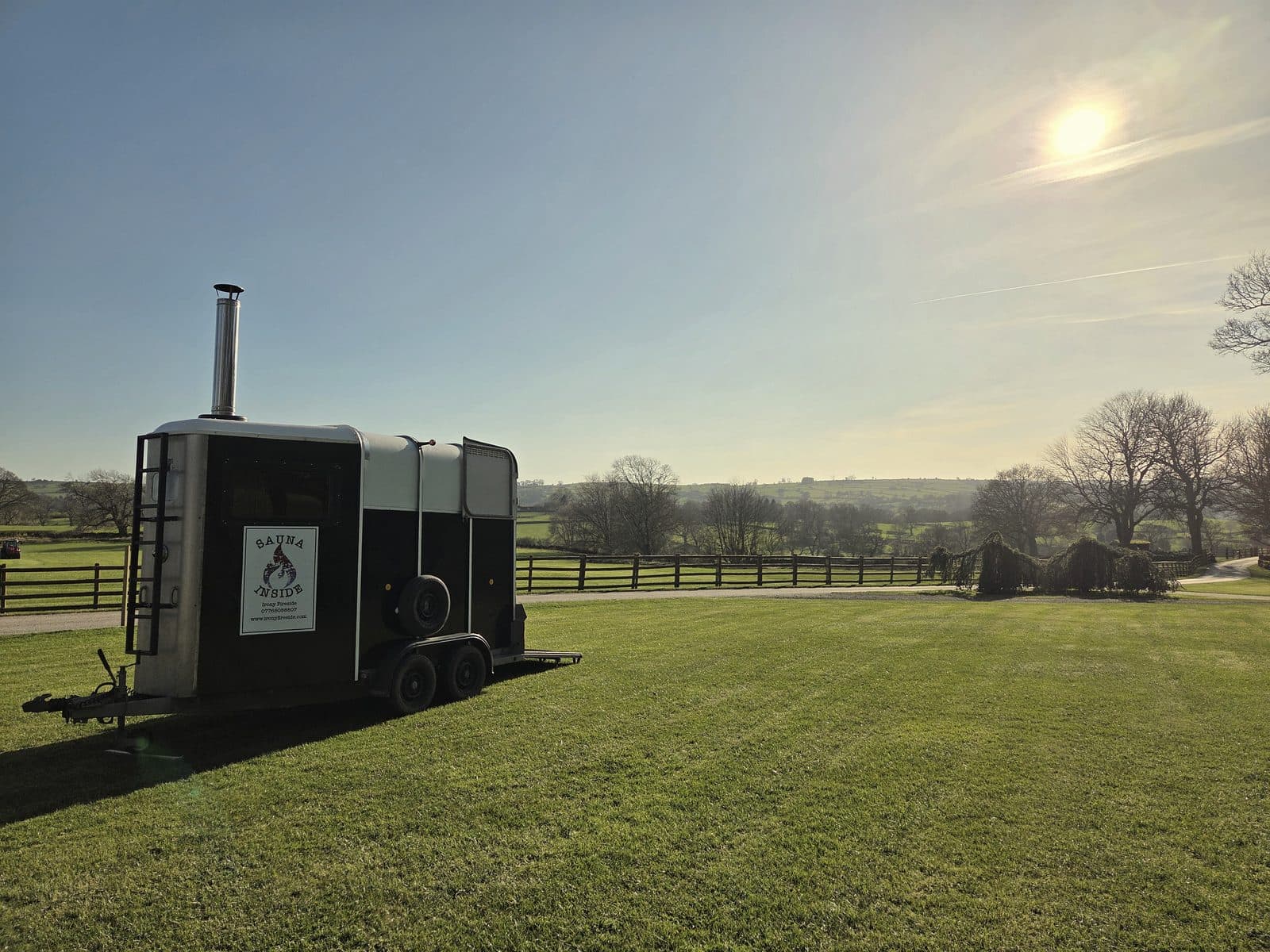 Converted horsebox sauna with chimney on green countryside lawn at sunset with rolling hills behind
