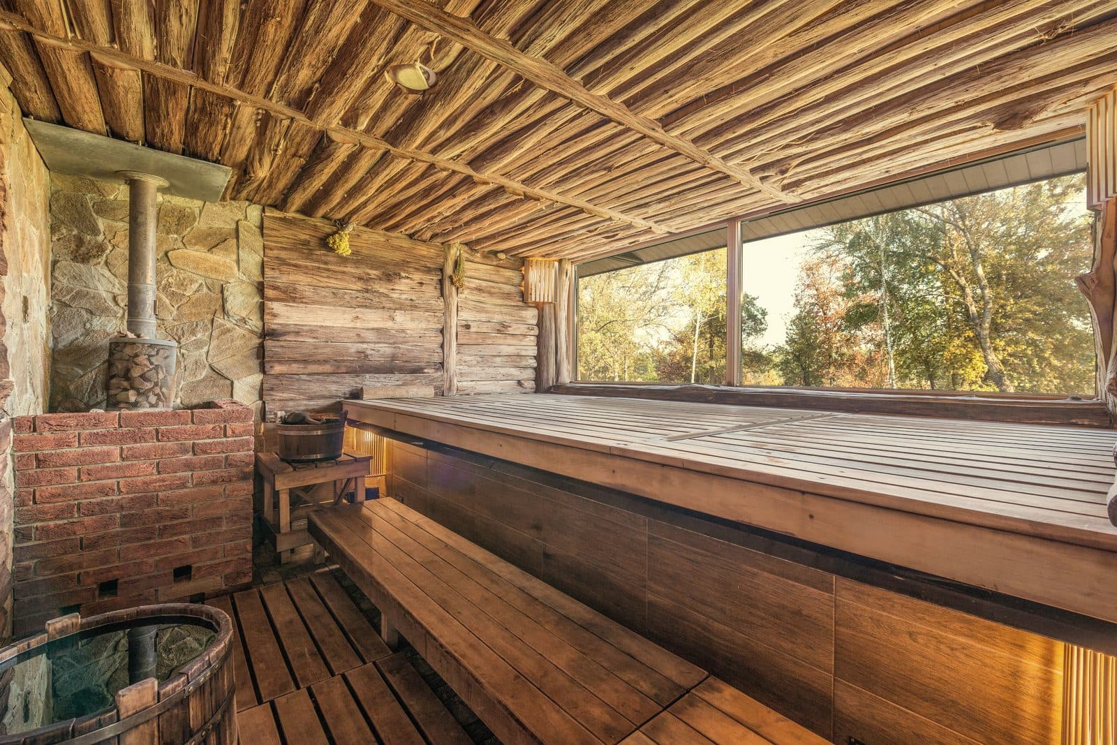 Rustic log-cabin sauna interior with a brick stove base and timber benches