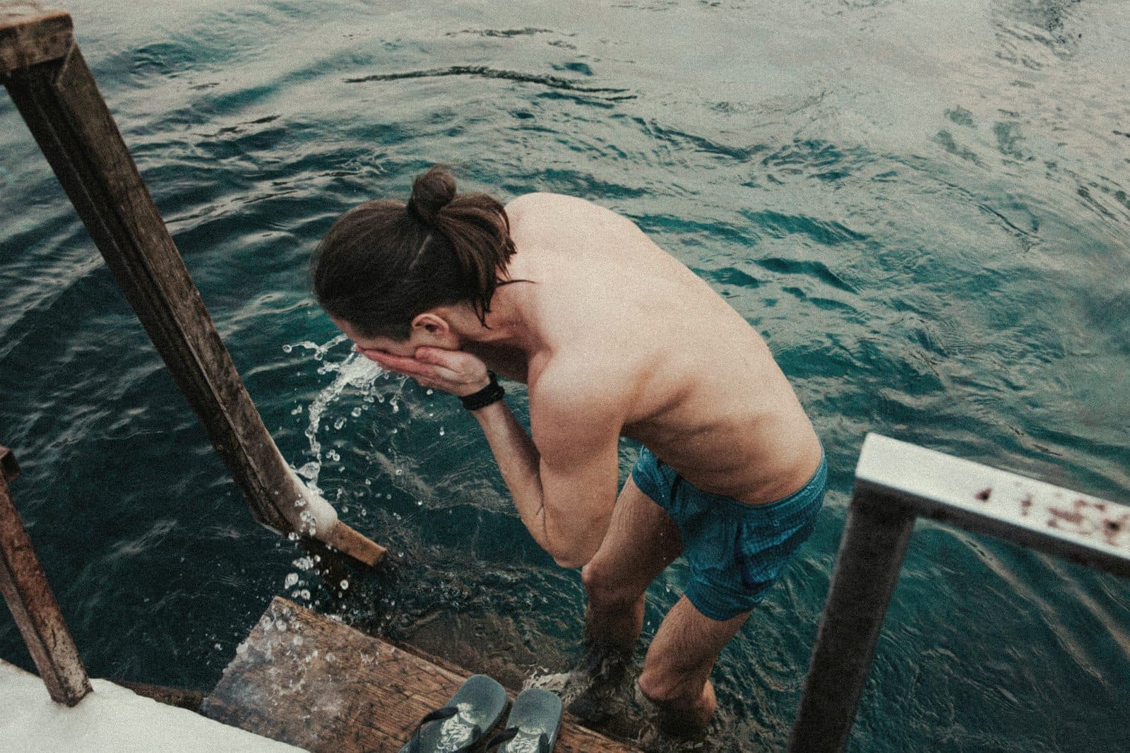 Person climbing out of cold open water on a wooden ladder after a sauna session