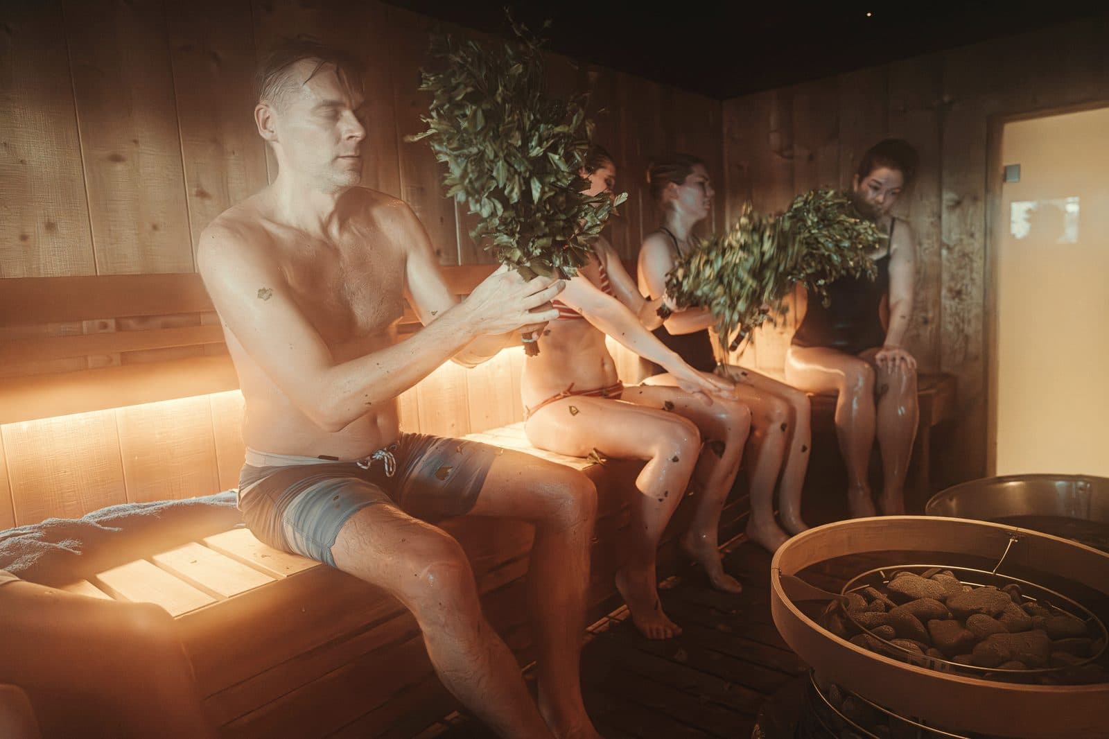 Group holding birch vihta whisks in a steam-filled sauna