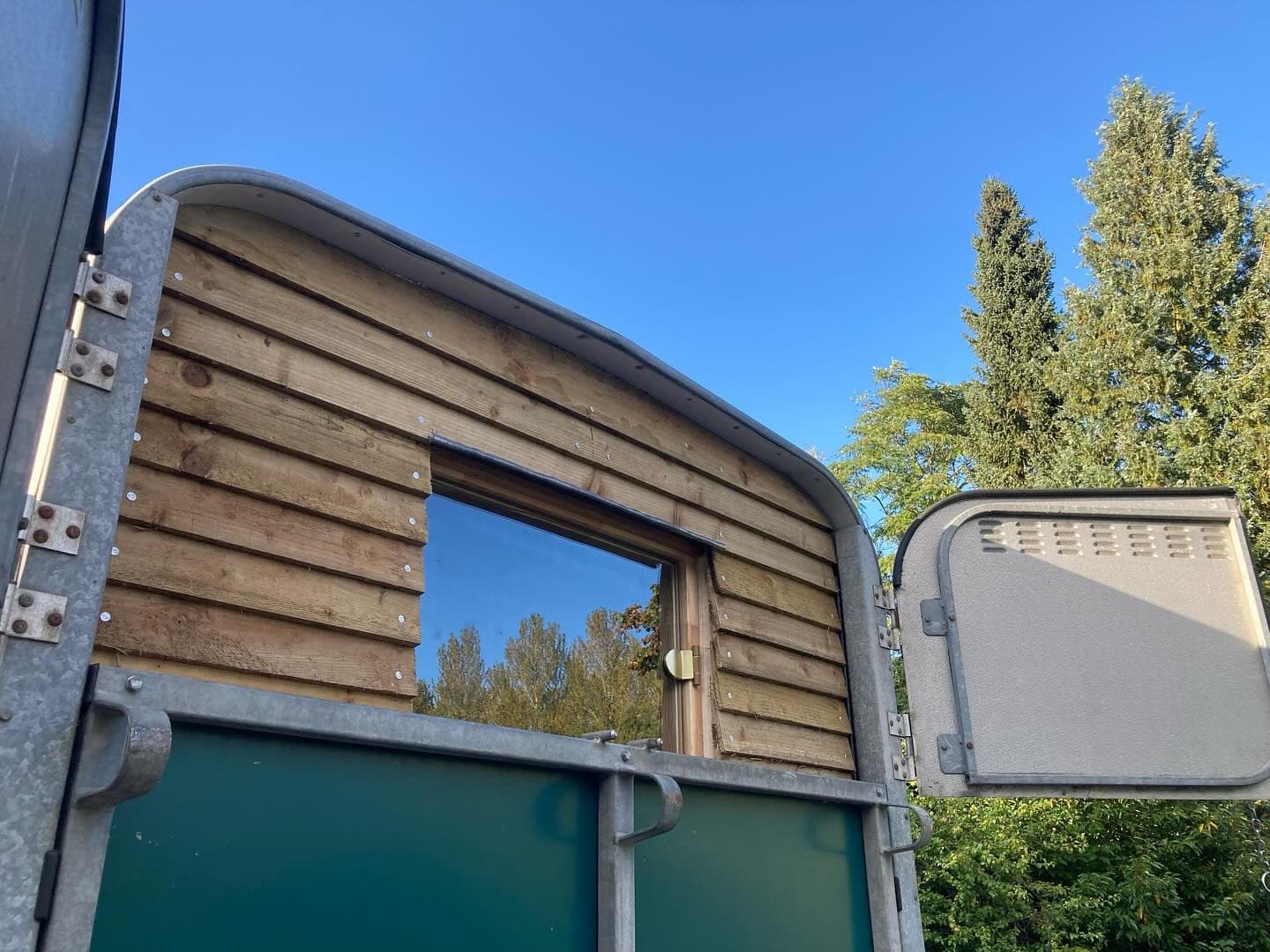 Detail of horsebox sauna conversion showing timber cladding and curved roof with blue sky behind