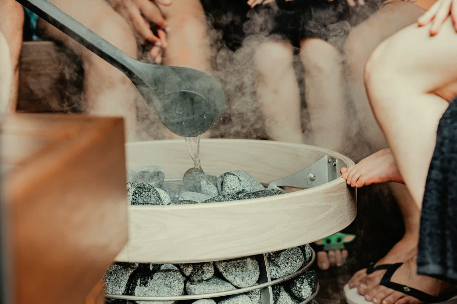 Water being poured on hot sauna stones from a wooden ladle