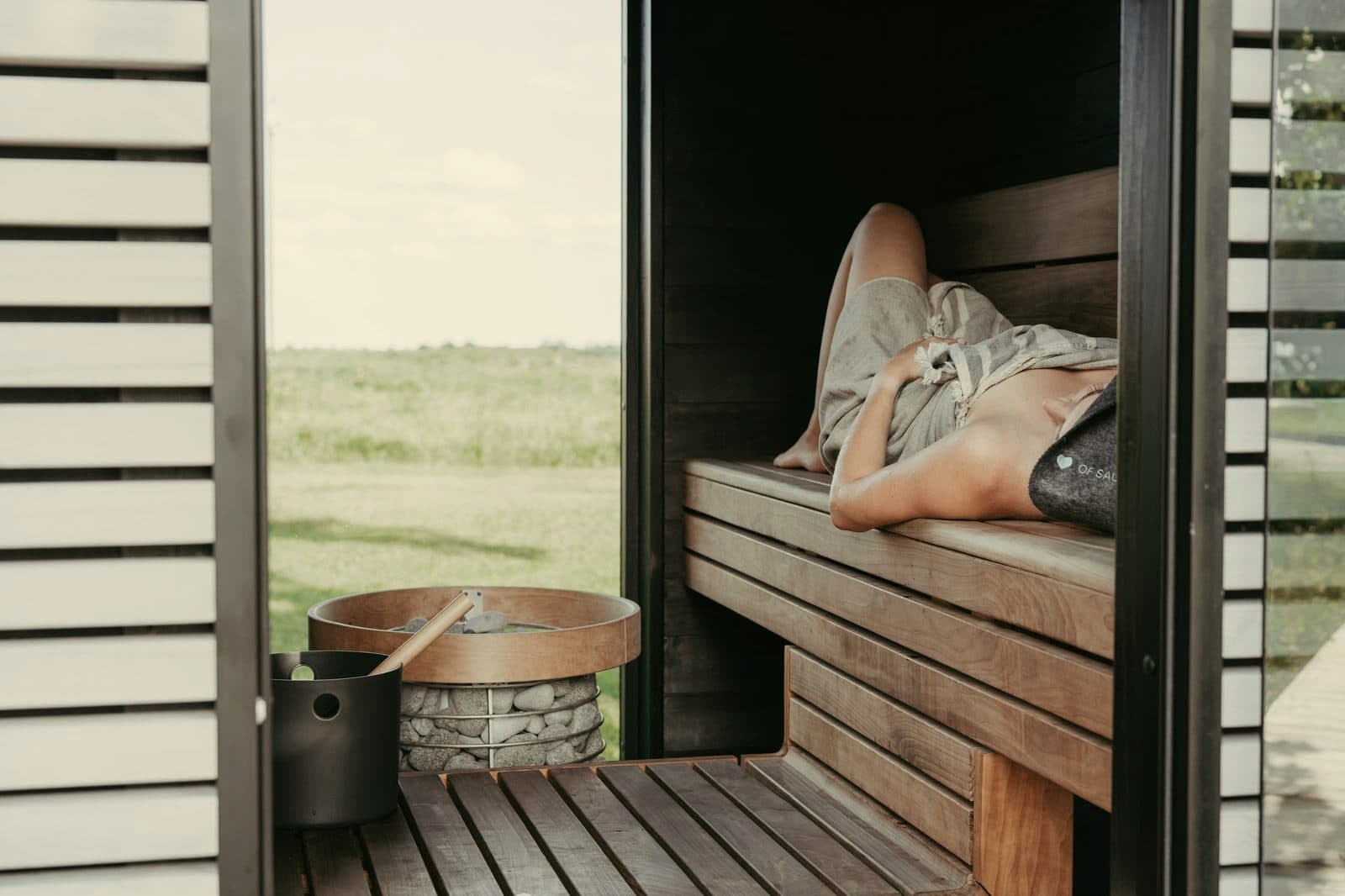 Person relaxing on a timber bench inside an outdoor sauna